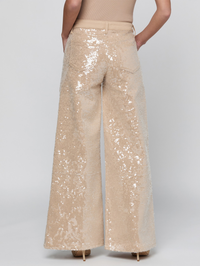 A person shown from the back wearing wide-leg sequined pants in a light champagne beige color, paired with a matching beige top and heels, against a light gray studio background.
