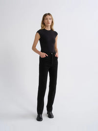 Full-length styled view of the AGOLDE Agata Bodysuit in Black with hands in the pockets of black jeans.