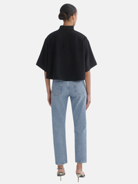 A model shown from the back wearing a black short-sleeved mock-neck top and light-wash blue jeans, standing against a light gray studio background.
