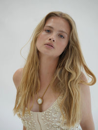 Model wearing the BOLOLA NYC Lola bolo necklace in gold with mother of pearl over a beaded ivory top.