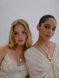 Two models in ivory, one wearing the BOLOLA NYC Lola bolo necklace in gold with mother of pearl.
