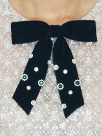 Close-up of black velvet bow embellishment with crystal and green stone detailing on the Long Sleeve Embellished Mini Dres…