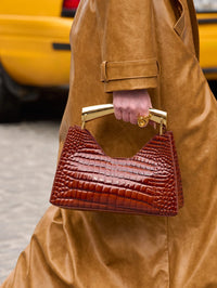 Street style view of the Bronx and Banco Poline croc embossed mini bag in Red carried by its gold handle.