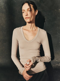 Editorial view of the Enza Costa Fluid Silk Rib Essential U Top in Light Grey against a dark textured wall.