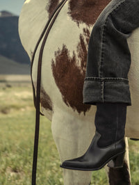 On horseback, the Freda Salvador Nancie Western Boot in Navy Suede Combo worn with cuffed black jeans.