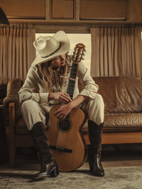 Seated model holding a guitar wearing the Freda Salvador Nancie Western Boot in Sable Suede Combo.