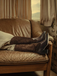 Legs crossed on a leather sofa in the Freda Salvador Nancie Western Boot in Sable Suede Combo.