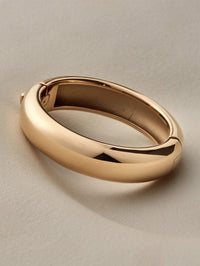 Angled view of the Jenny Bird Gemma Bangle in high polish gold on a soft neutral backdrop.