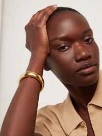 Model wearing the Jenny Bird Gemma Bangle in high polish gold on her raised wrist.