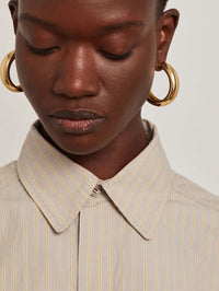 Model wearing a pair of Jenny Bird Large Gia Hoops in high polish gold with a striped shirt.