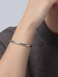 Model wearing the Jenny Bird Remi Bangle in two-tone on her wrist with a grey knit sweater.