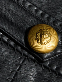 Close-up of the gold lion button and whip-stitching on the L'AGENCE Arlena Vegan Leather Mini Skirt in Black.
