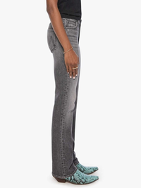 Side view of a person wearing gray denim jeans with a black top and green snakeskin-patterned pointed-toe flats, against a plain white background.