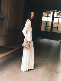 Model in a cream maxi dress carrying the NAGHEDI Gramercy Bucket in Carmel in a stone archway.