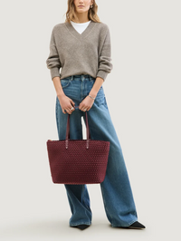 Front view of the Jetsetter Small Tote in Bordeaux by Naghedi, styled with a gray V-neck sweater