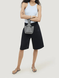 Model wearing the NAGHEDI Kyoto Clutch Satin in Graphite on her wrist with a pale blue tank.