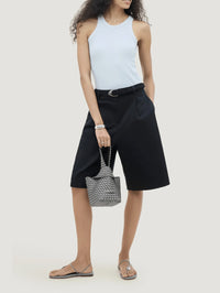 Model carrying the NAGHEDI Kyoto Clutch Satin in Graphite by hand with black tailored shorts.