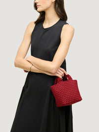 Model carrying the NAGHEDI St. Barths Petit Tote in Rosso by its top handles with a black sleeveless dress.