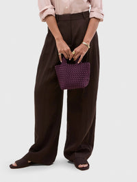 Model holding the NAGHEDI St. Barths Petit Tote Satin in Bisou with brown wide leg trousers.