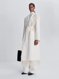 Angled full-length view of the SIMKHAI Carrie Fringe Coat in Frost with fringe at the hem.