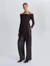 Three quarter view of a model wearing the SIMKHAI Corrine Leather Pant in Dark Chocolate, hand in pocket