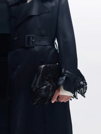 Styled view of the SIMKHAI Pia Beaded Fringe Clutch in Black carried by hand against a black trench coat.