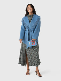 Full-length view of the SIMKHAI Rowen Fringe Jacket in Dusty Blue styled with a plaid midi dress.