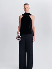 Front view of a model in the SIMKHAI Scarlett Draped Velvet Cape Top in Black with black wide leg trousers.