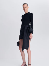 Three-quarter view of the SIMKHAI Tedda Taffeta Knit Mini Dress in Black showing the asymmetric sash.