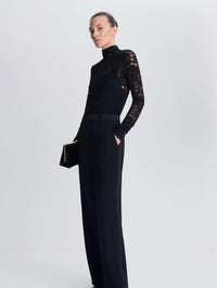 Three-quarter view of the SIMKHAI Zurie Lace Bodysuit in Black styled with black trousers and a clutch.