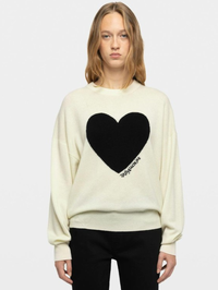 A model wearing a cream-colored crewneck sweatshirt with a large black heart on the front and the brand name zadig and voltaire printed in black script along the bottom edge of the heart.