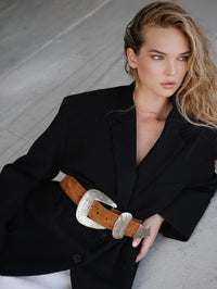 Seated model in a black blazer belted with the Streets Ahead Braun Belt in tan suede