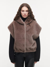 Front view of the STUDIO AR Olena Reversible Faux Fur Gilet in Pebble with hood, worn over a black knit
