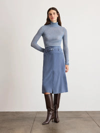 Front view of the Tanya Taylor Beacon Skirt in Morning Fog, a belted blue suede midi, styled with tall brown boots.