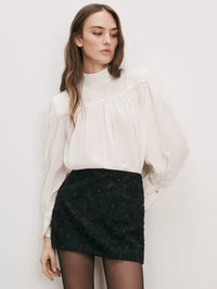 Front view of the Veronica Beard Brooks Mock-Neck Blouse in Dove White tucked into a black beaded mini skirt.