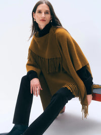 Seated front view of the White + Warren Cashmere Blend Fringe Poncho in Antique Gold over a black turtleneck