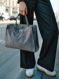 Street shot of the Zadig & Voltaire Jack Suede Bag in Road grey carried by hand with pinstripe trousers.